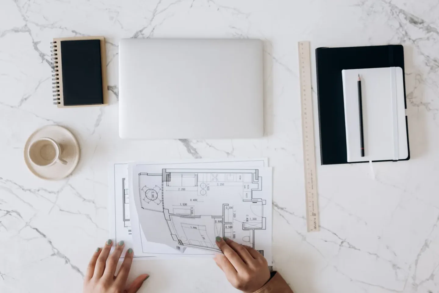 Reviewing and marking a printed 2D CAD technical drawing with dimensions alongside a laptop